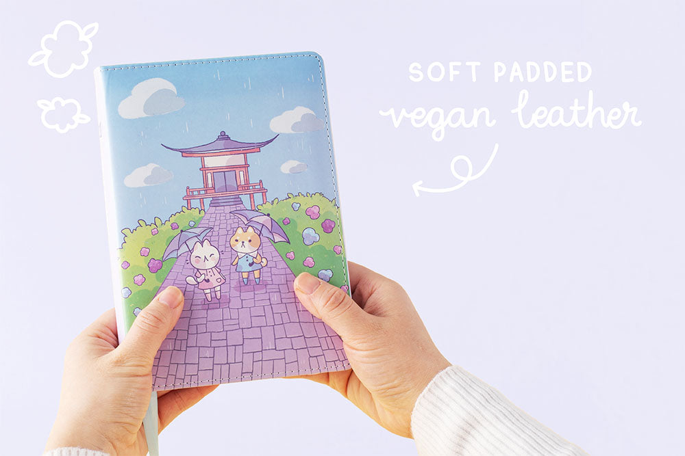 Tsuki Four Seasons: Summer Edition Bullet Journal with soft padded vegan leather cover designed with @milkkoyo held in hands in lilac background