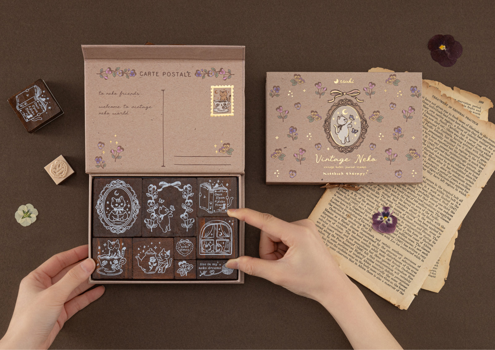 A person's hands opening the Vintage Neko stamp box, revealing the detailed wooden stamps inside, set against a dark brown background.