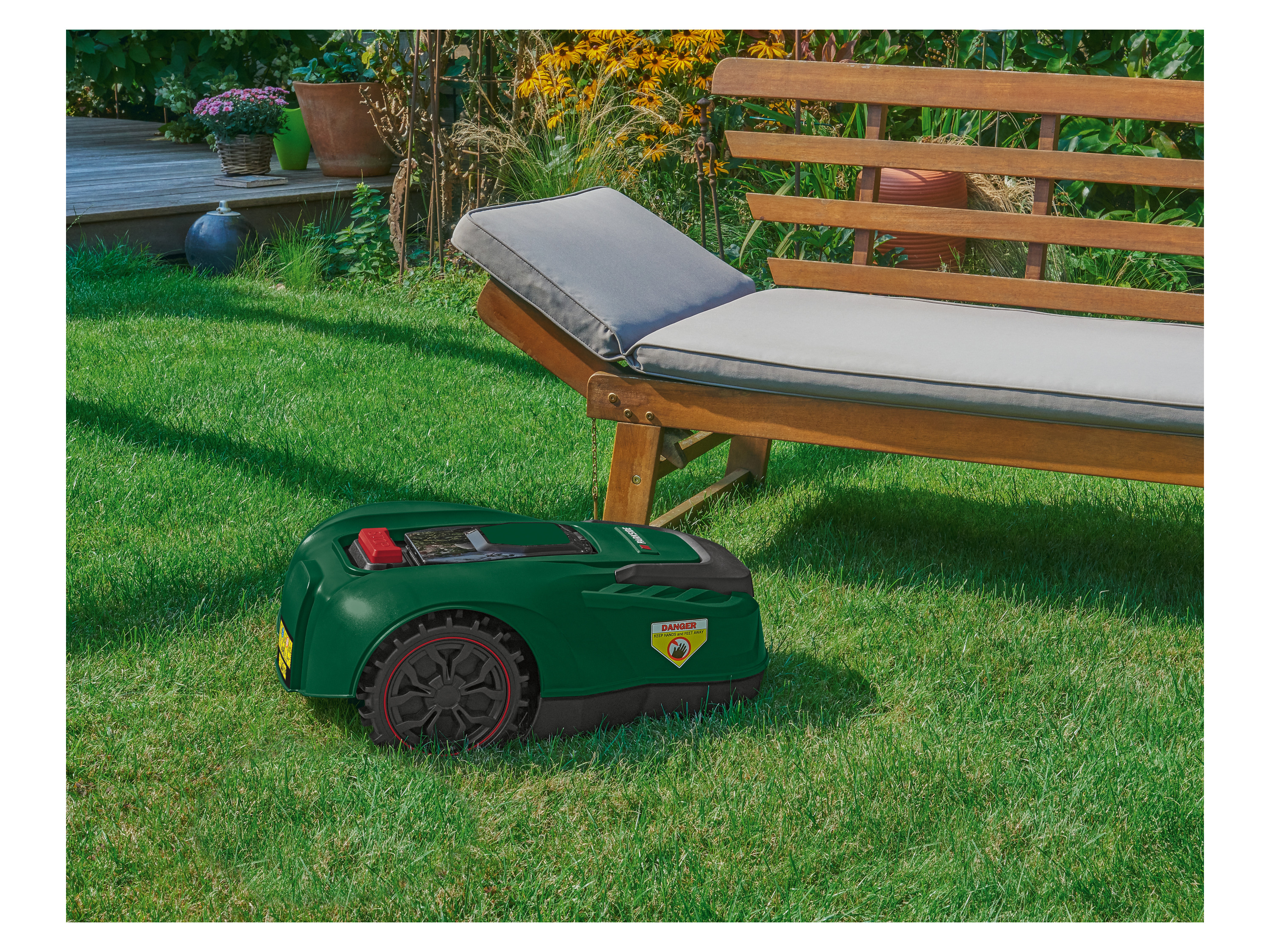 Tondeuse robot Gardena sur pelouse verte près de meubles de jardin.